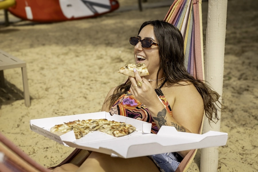Une vacancière en train de déguster une pizza artisanale dans un espace de restauration en plein air