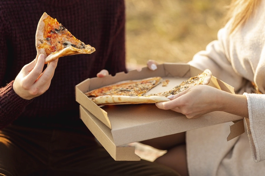 Vacanciers partageant une pizza en boîte en extérieur, illustrant l'offre de snacking proposée dans les campings