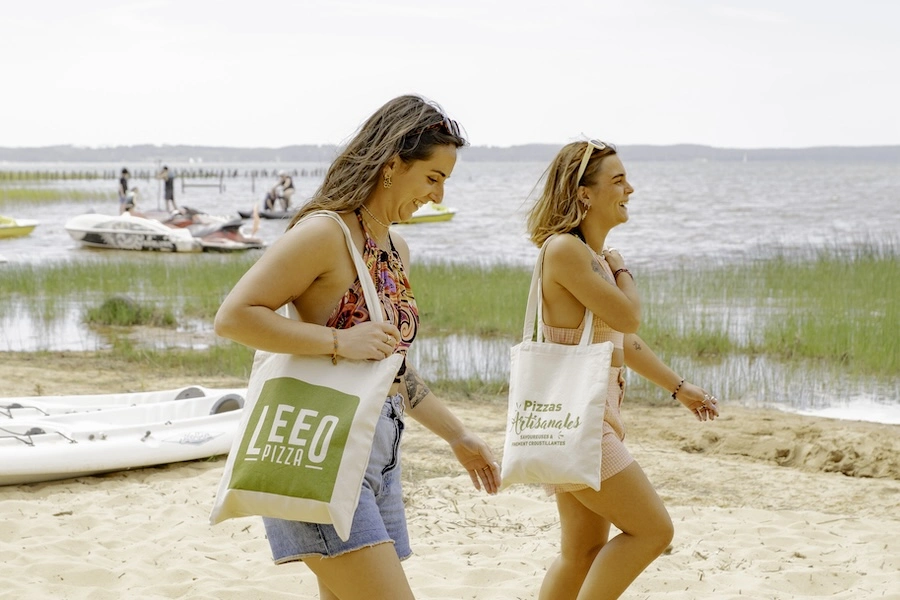 Deux vacancières sur une plage de camping portant des tote bags Leeo Pizza
