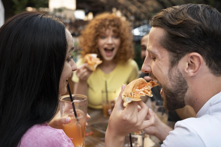 Groupe de vacanciers dégustant une pizza ensemble en extérieur, moment de partage et de convivialité en soirée
