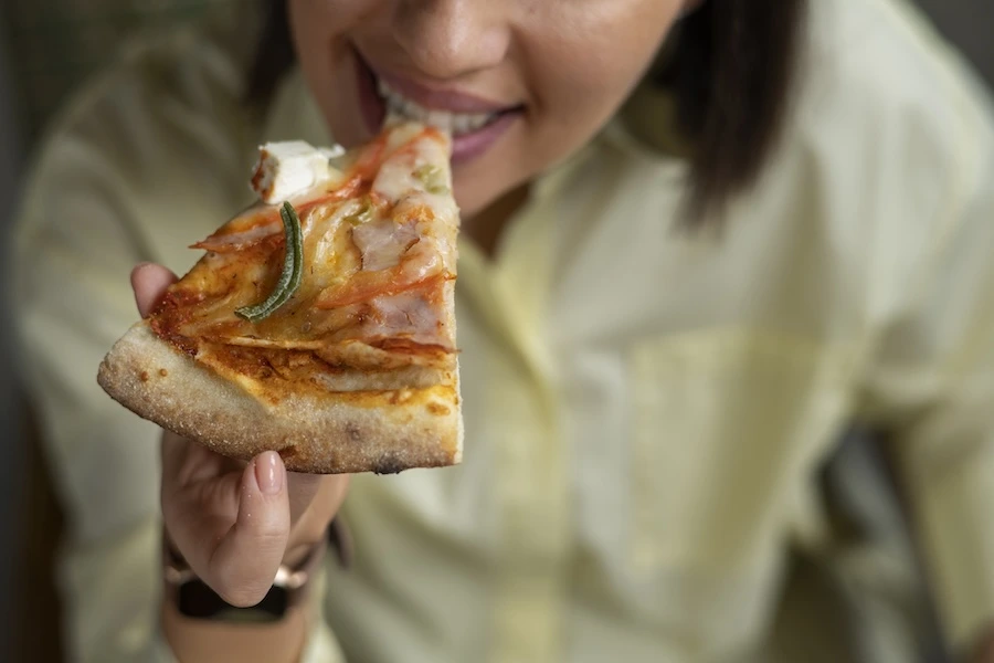 Gros plan sur une part de pizza artisanale généreusement garnie, dégustée par une vacancière, illustration d'une offre de pizza prête à cuire en camping