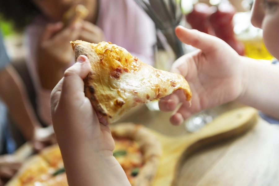 Part de pizza artisanale tenue par un enfant lors d'un repas convivial en camping, produit apprécié de toutes les nationalités